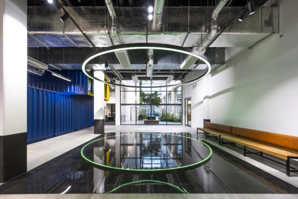 Moderne entreehal aan de Kabelweg met industriële elementen, een groot lichtgevend cirkelvormig kunstwerk en een reflecterende zwarte vloer.