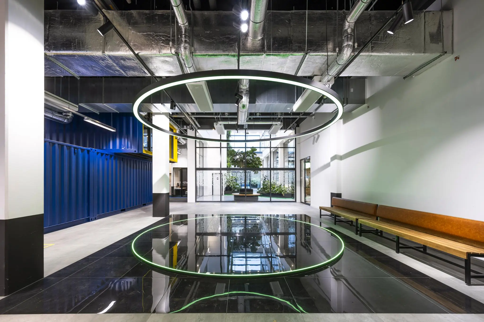 Moderne entreehal aan de Kabelweg met industriële elementen, een groot lichtgevend cirkelvormig kunstwerk en een reflecterende zwarte vloer.