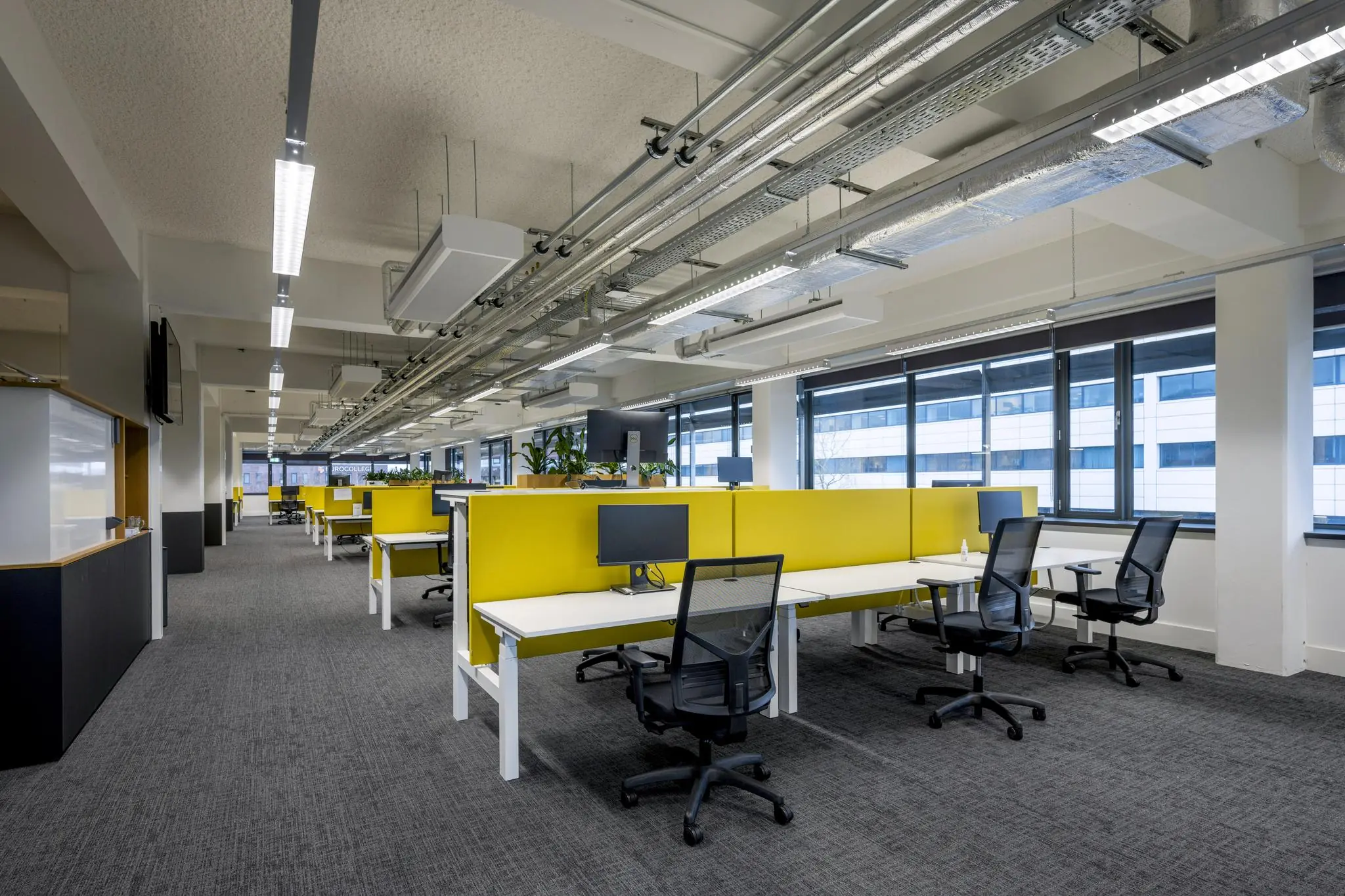 Modern kantoorinterieur aan de Kabelweg met open werkplekken en gele scheidingspanelen.