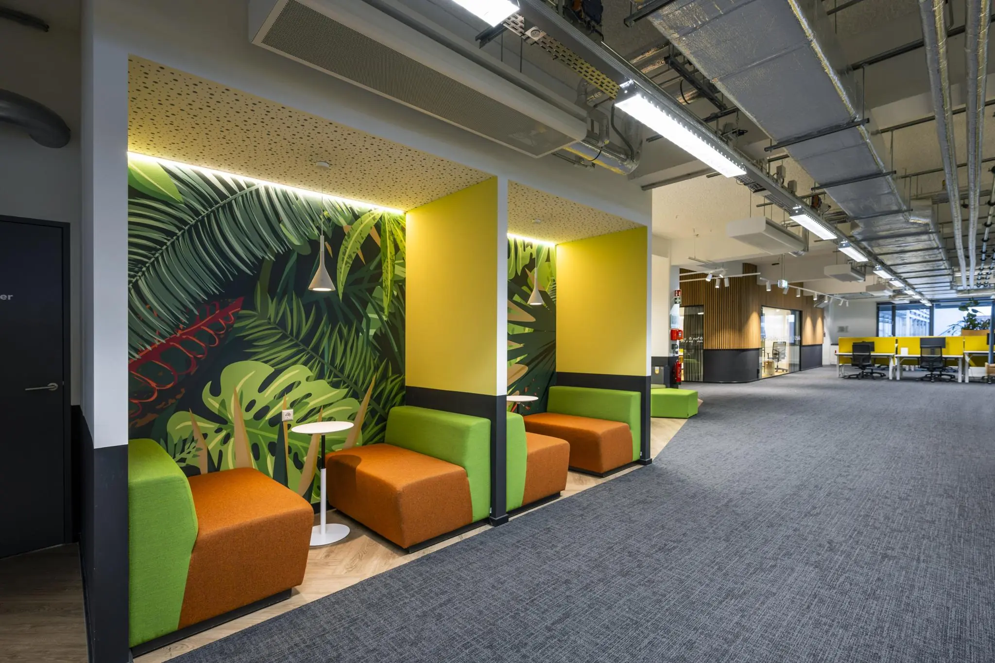 Moderne kantoorruimte aan de Kabelweg met kleurrijke zitnissen, tropisch wanddesign en open werkplekken.