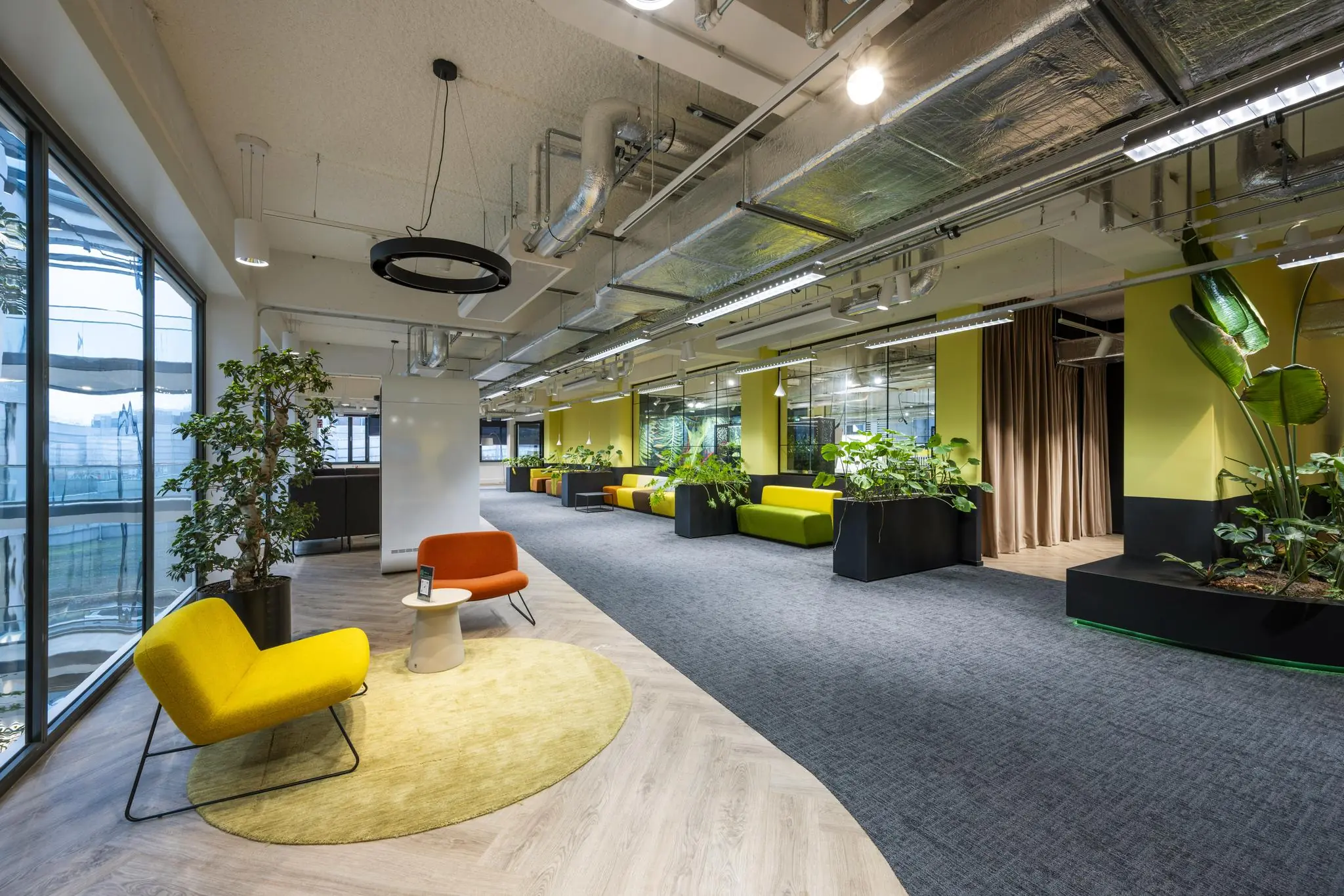Modern ingerichte kantoorruimte aan de Kabelweg met kleurrijke zitplekken, veel planten en industriële plafondafwerking.
