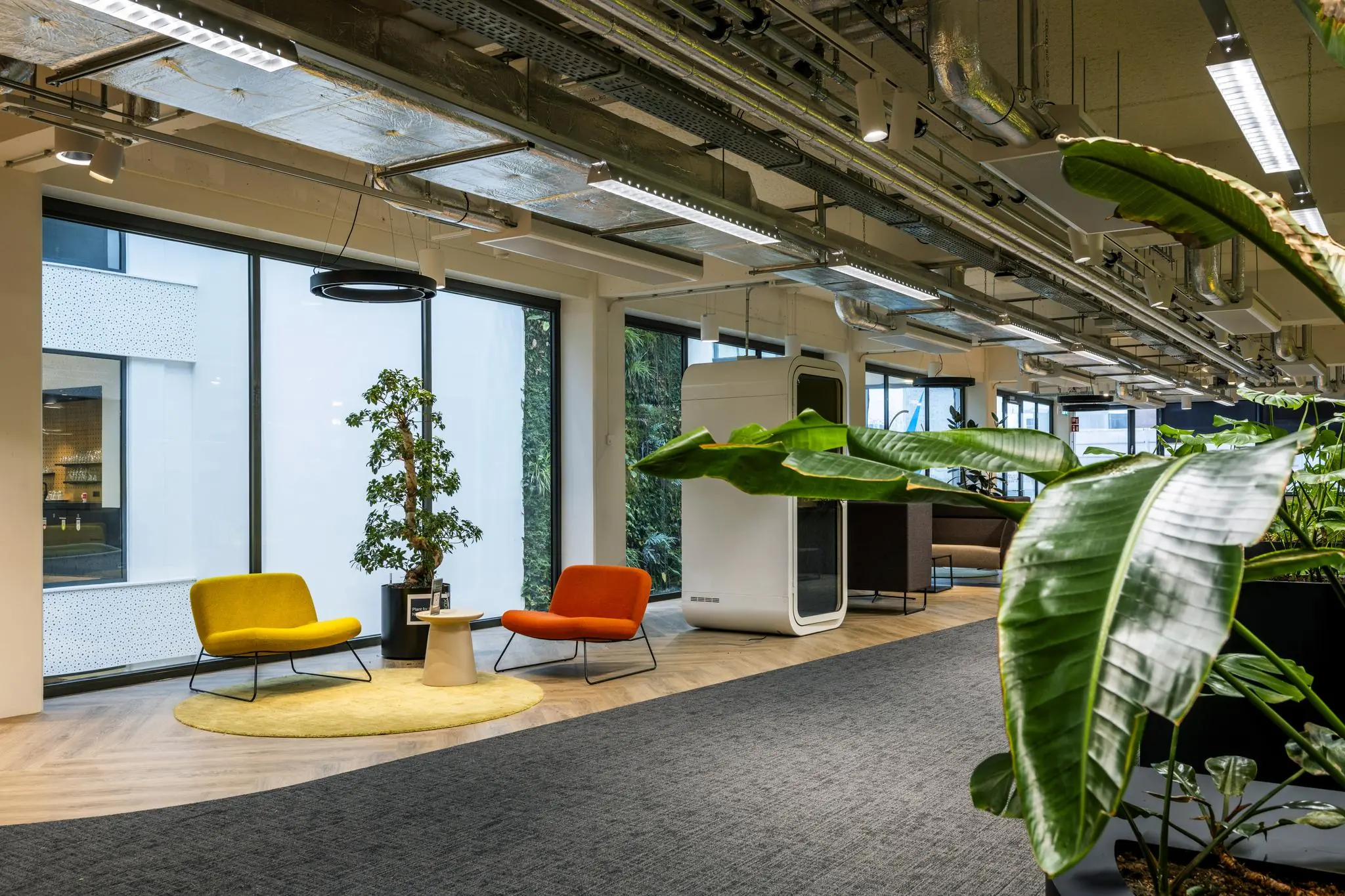 Moderne kantoorruimte aan de Kabelweg met kleurrijke zitjes, grote planten en een belcel.