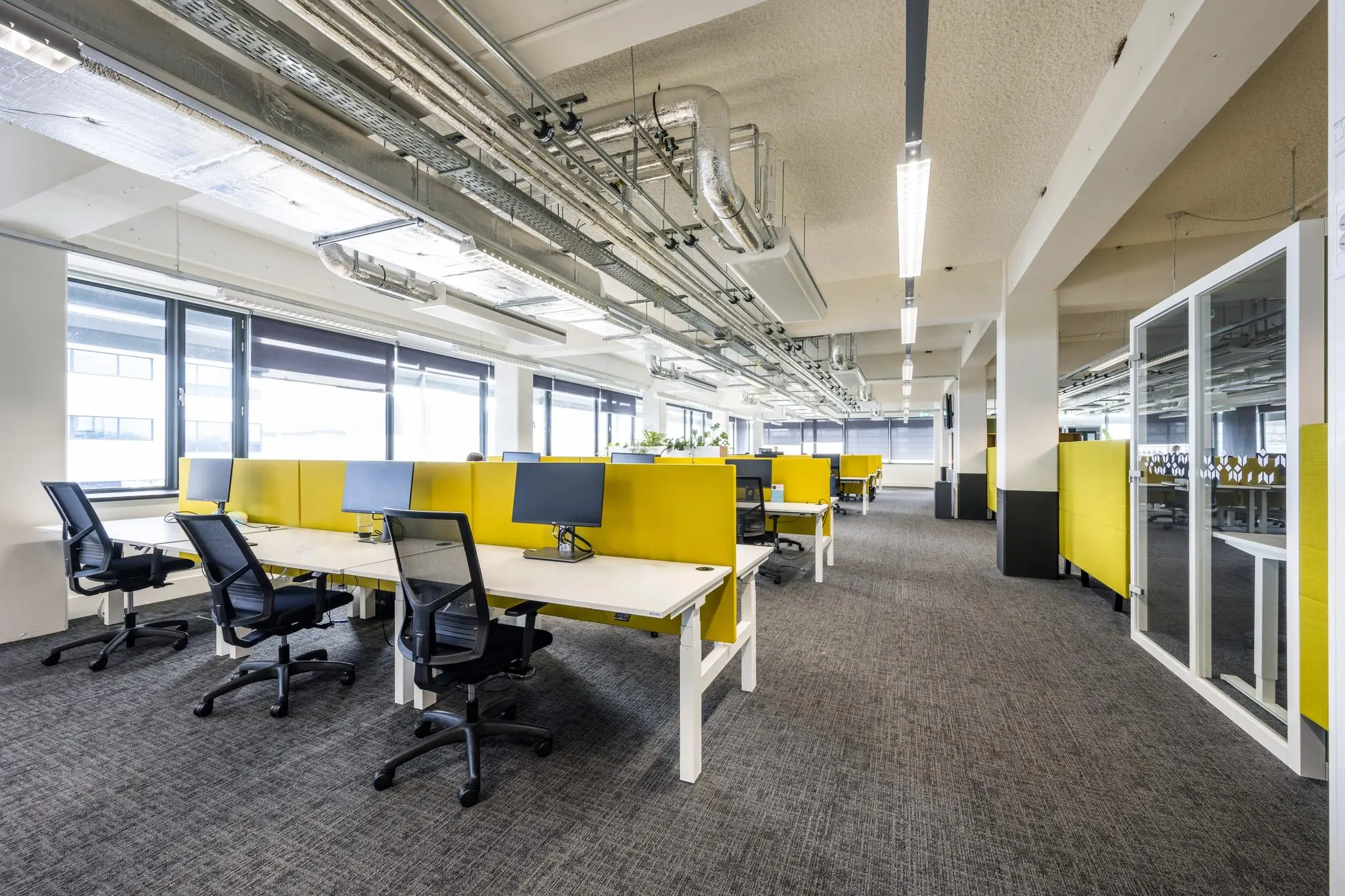 Modern kantoorinterieur aan de Kabelweg met open werkplekken, gele scheidingspanelen en bureaus met computerschermen.