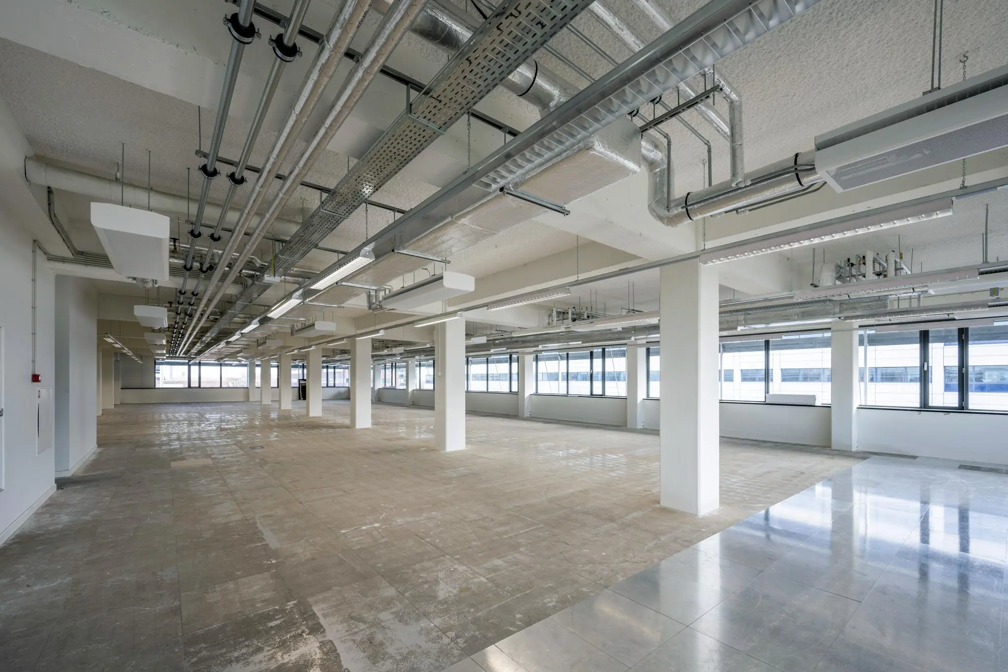 Leeg kantoorpand aan de Kabelweg met zichtbare leidingen, pilaren en grote ramen.
