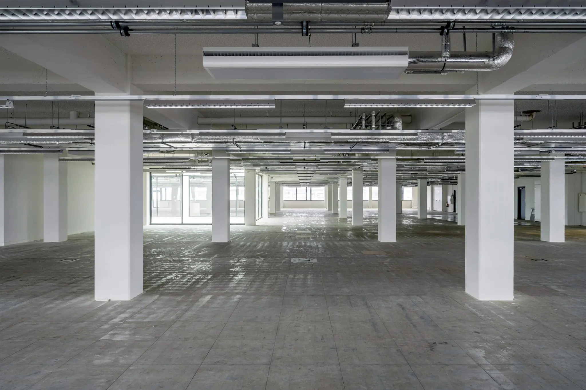 Leeg kantoorpand aan de Kabelweg met betonnen vloer, witte pilaren en zichtbare plafondinstallaties.