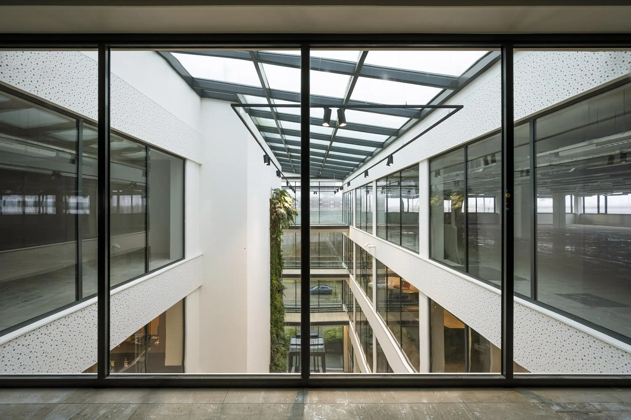 Modern glazen atrium in kantoorgebouw aan de Kabelweg met zicht op meerdere verdiepingen en groene wand.
