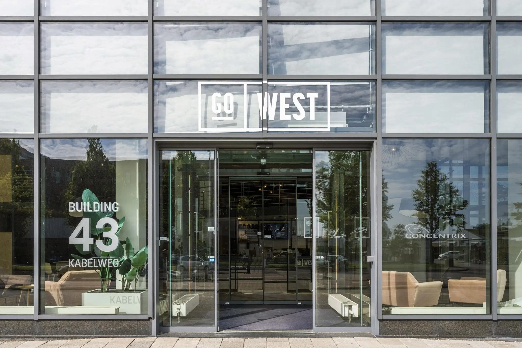 Ingang van gebouw 43 aan de Kabelweg met de tekst "GO WEST" boven de deur en "Concentrix" zichtbaar op het raam.