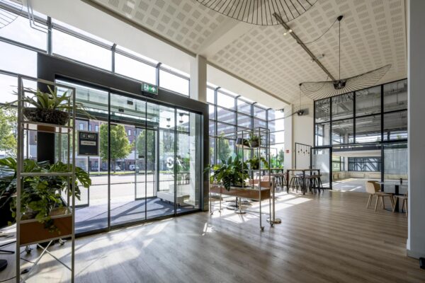 Moderne, lichte entreehal van een kantoorgebouw aan de Kabelweg met glazen gevel, planten en zithoeken.