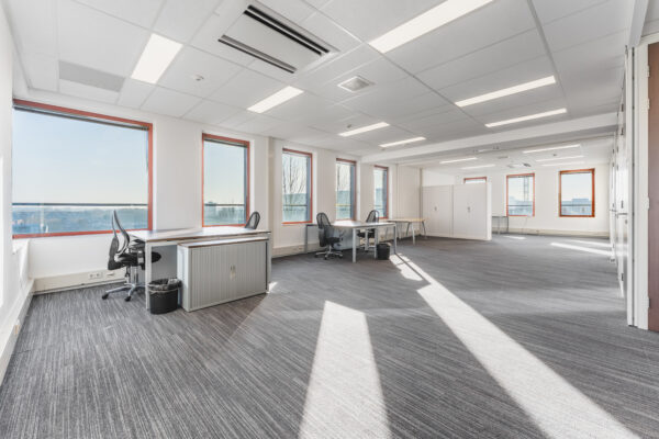 Een ruime en lichte kantoorruimte met grote ramen en bureaus.