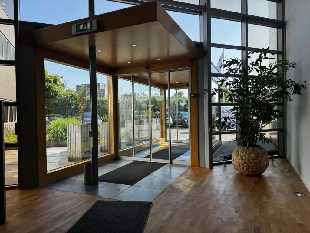 Ingang van een modern kantoorgebouw aan de Softwareweg met glazen schuifdeuren, houten vloer en een grote plantenbak.