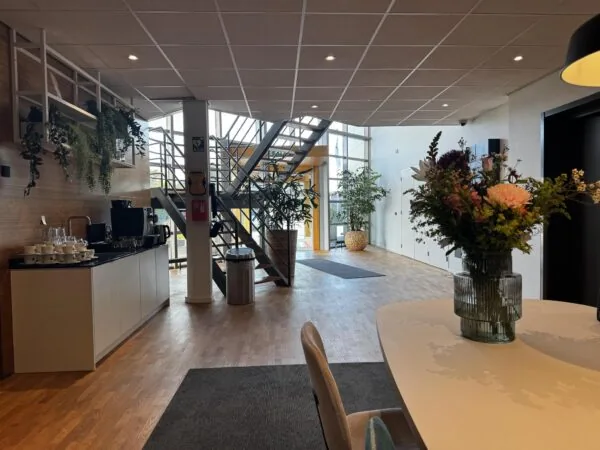 Moderne kantoorentree met een koffiecorner, bloemen op tafel en een trap naar de bovenverdieping bij Softwareweg.