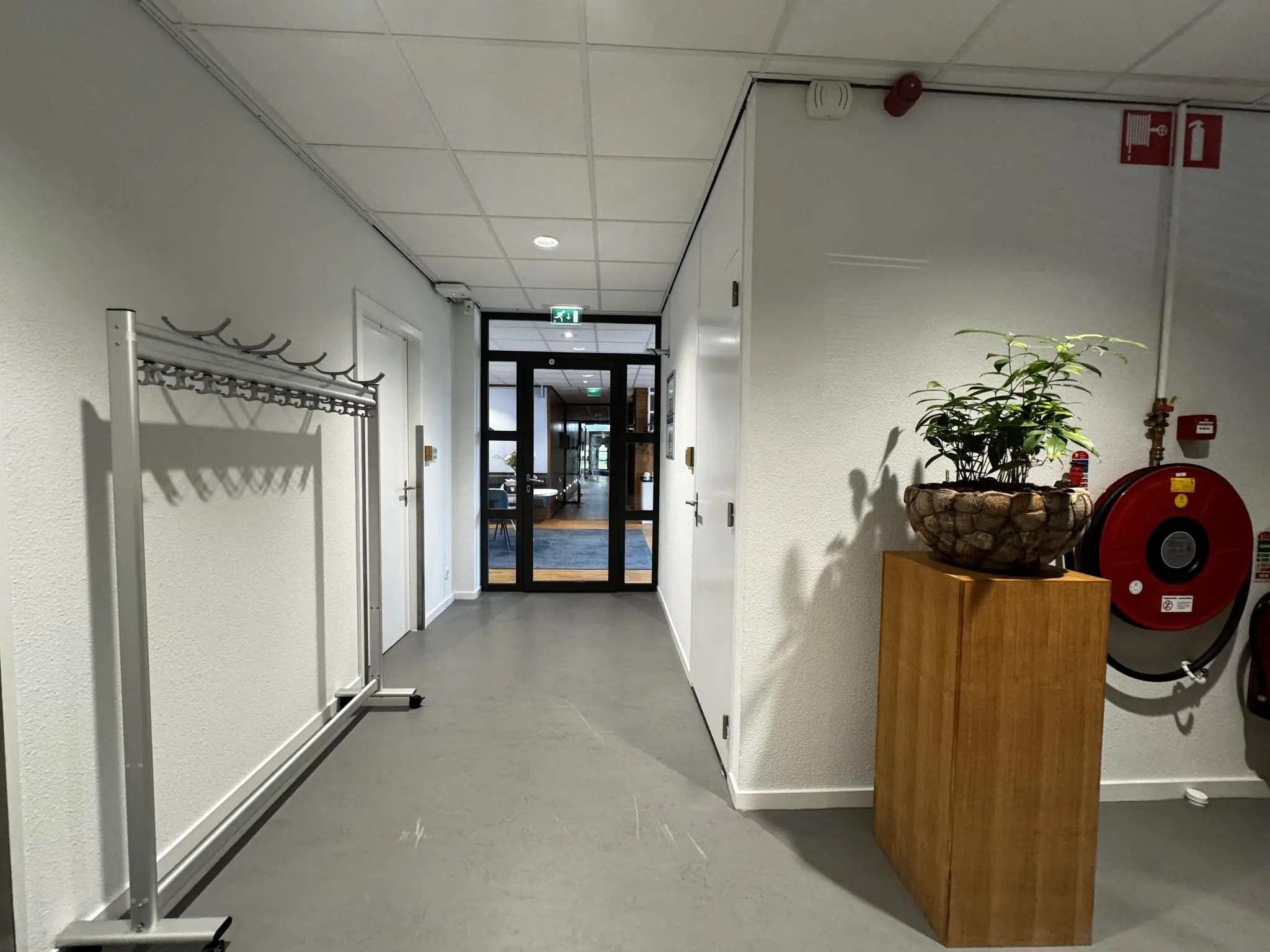 Hal met een kapstok, een plant op een houten zuil en een brandslanghaspel bij de uitgang naar een kantoorruimte aan de Softwareweg.