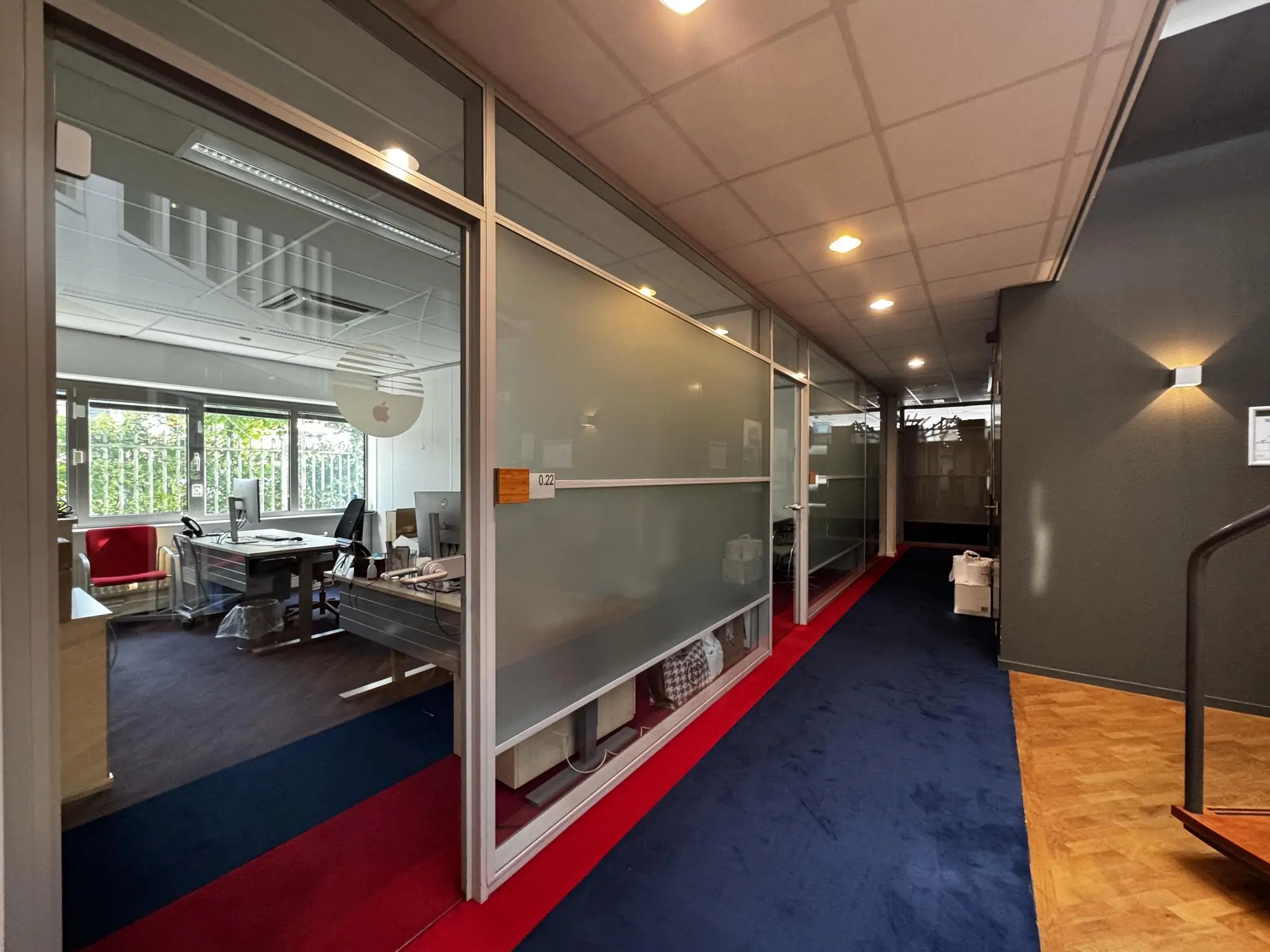 Gang met zicht op een modern kantoor aan de Softwareweg, met glazen wanden en kleurrijk tapijt.