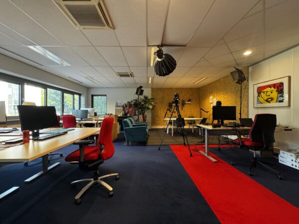 Moderne kantoorruimte aan de Softwareweg met werkplekken, studioapparatuur en een rode loper op donkerblauw tapijt.
