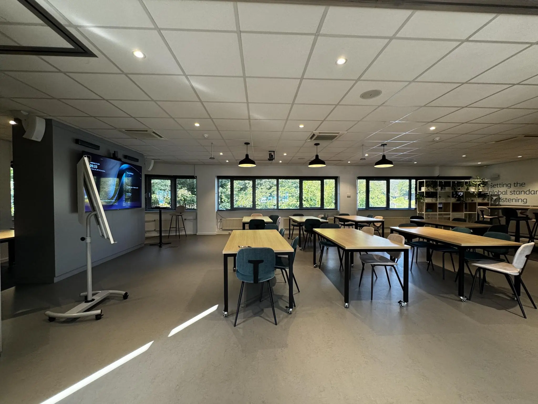 Moderne vergaderruimte op Softwareweg met meerdere tafels, stoelen, een scherm en veel daglicht.
