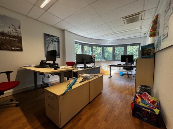 Kantoorruimte aan de Softwareweg met meerdere bureaus, kantoorstoelen, computerschermen en een groot raam met uitzicht op groen.