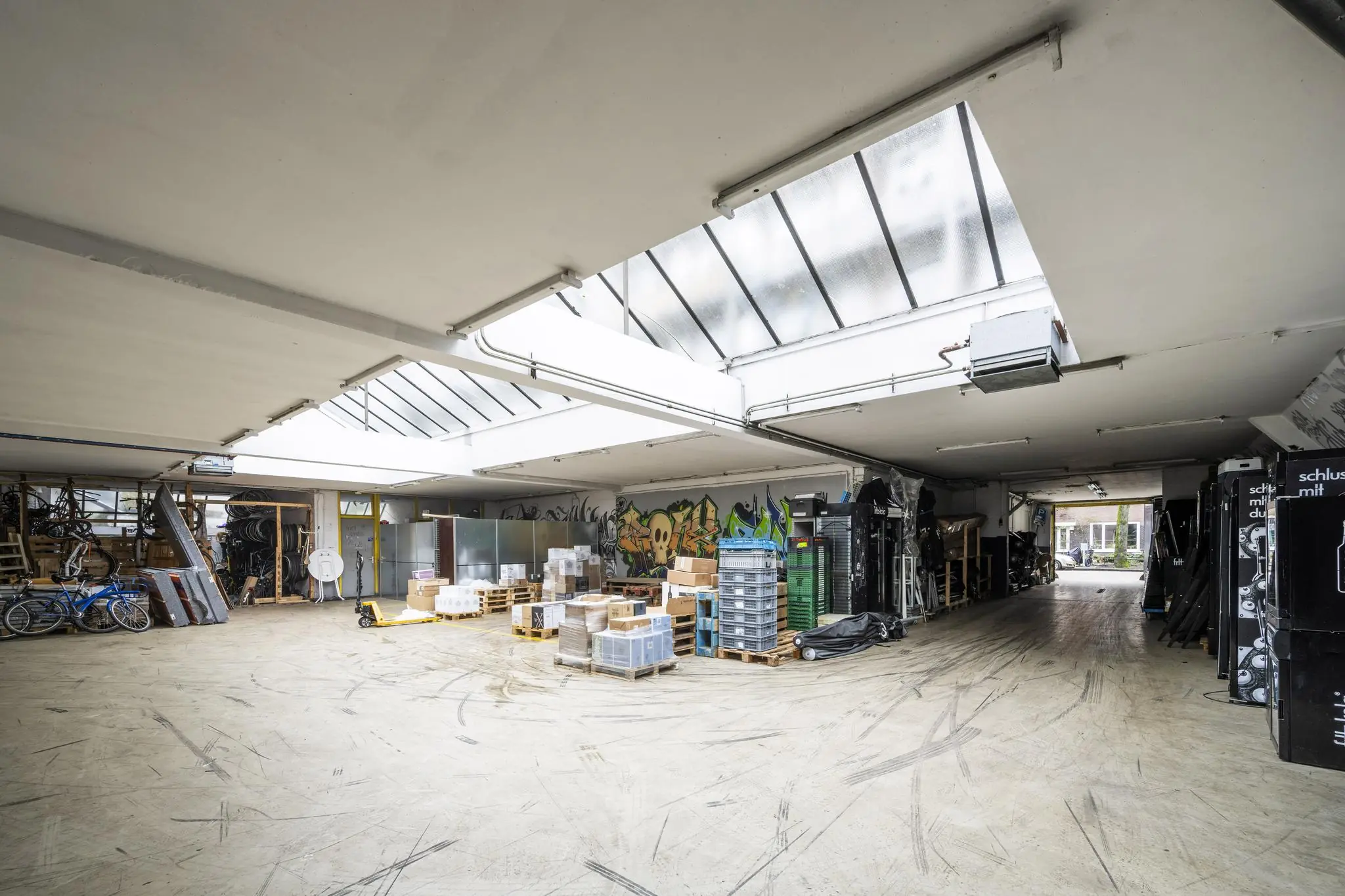 Ruime industriële opslagruimte aan de Baarsjesweg met skylights, graffiti op de muur en gestapelde materialen op pallets.