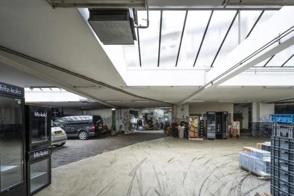 Overdekte binnenplaats aan de Baarsjesweg met geparkeerde auto's, fietsen, apparatuur en fritz-kola koelkasten.