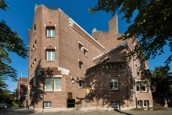 Bakstenen hoekgebouw aan het Emmaplein met opvallende geveldetails en witstenen accenten, gefotografeerd op een zonnige dag.