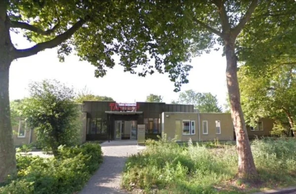 Gezondheidscentrum Tandem in een groene, boomrijke omgeving met een betegeld pad naar de ingang.