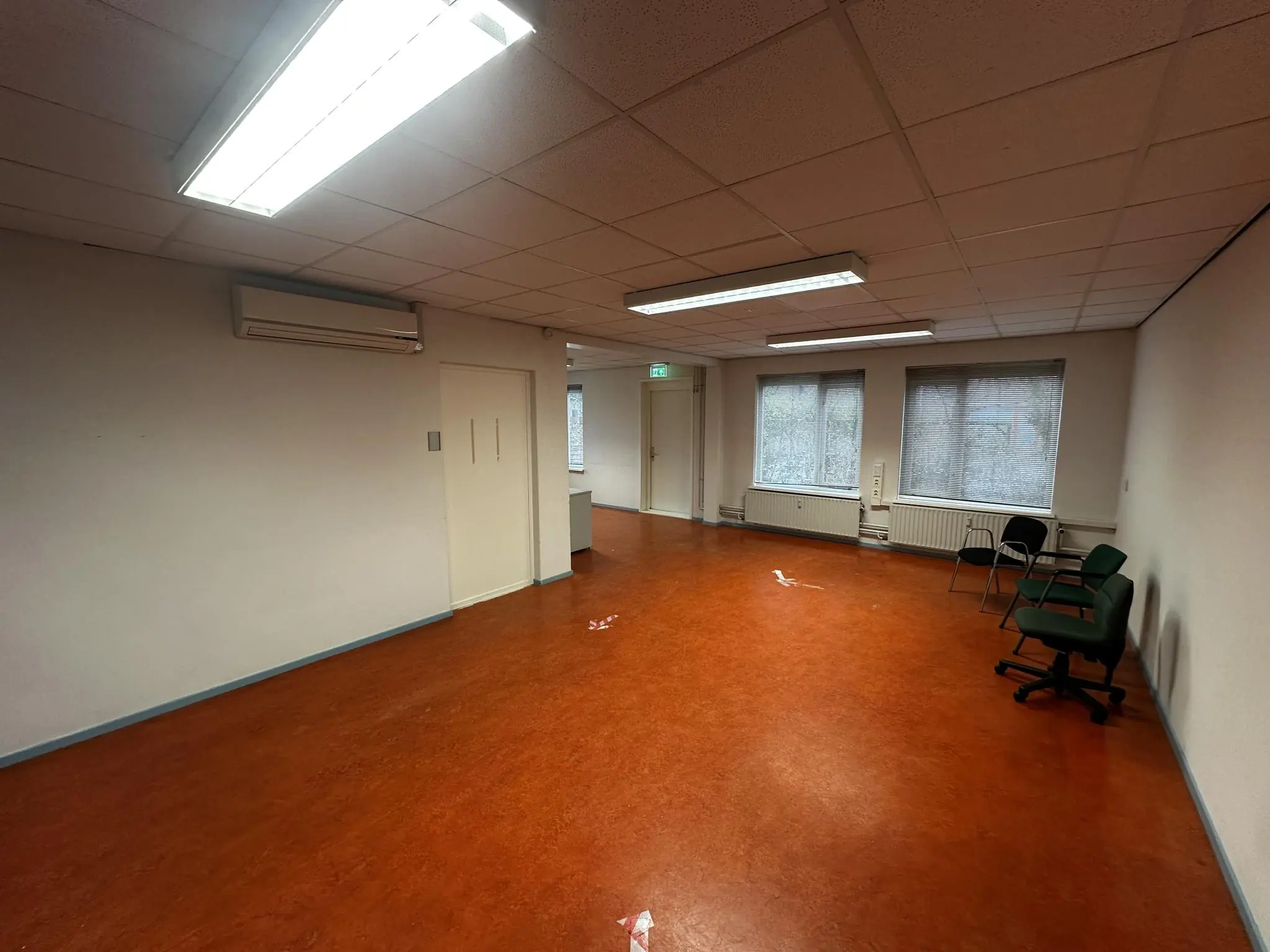 Lege binnenruimte van Veulenkamp met roodbruine vloer, witte muren, bureaustoelen en tl-verlichting.