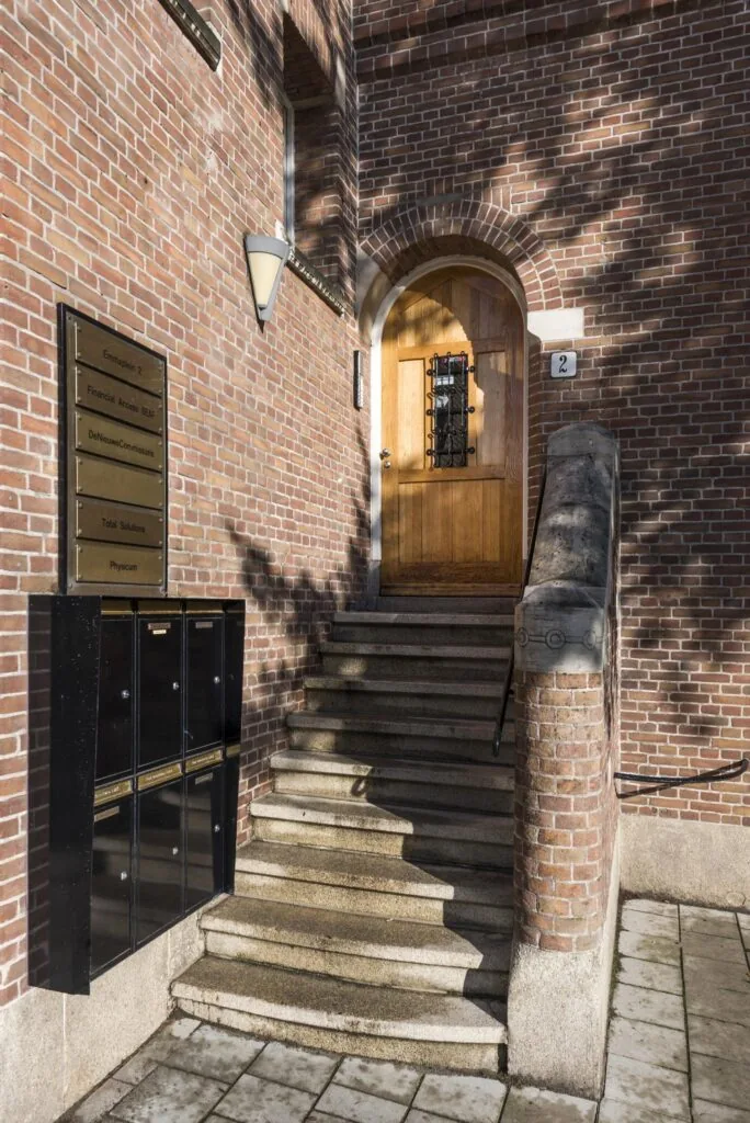 Ingang met stenen trap en houten deur van Emmaplein 2, met bedrijfsnaambord en brievenbussen aan de muur.