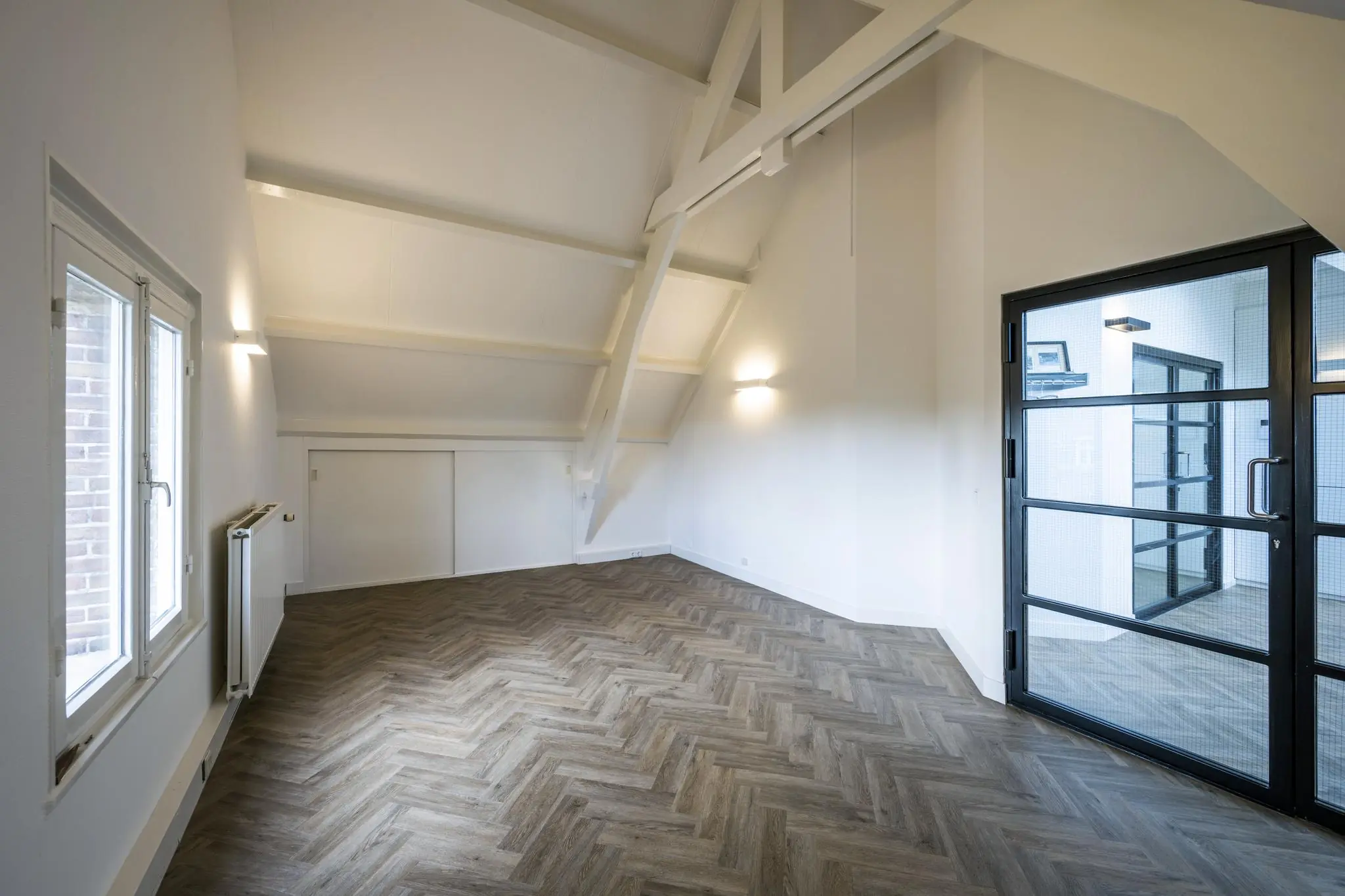 Lichte zolderkamer op het Emmaplein met visgraatvloer, hoge schuine wanden en een zwarte stalen glazen deur.