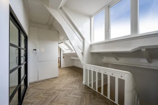 Bovenverdieping van een woning aan het Emmaplein met visgraatvloer, witgeschilderde balken en grote ramen met veel lichtinval.