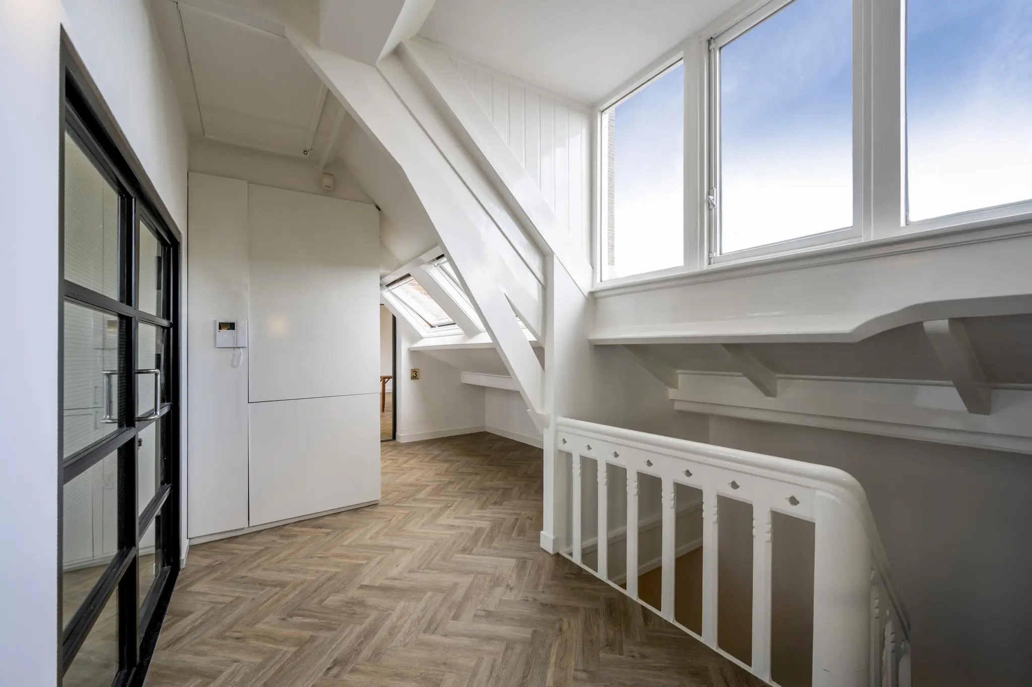 Bovenverdieping van een woning aan het Emmaplein met visgraatvloer, witgeschilderde balken en grote ramen met veel lichtinval.