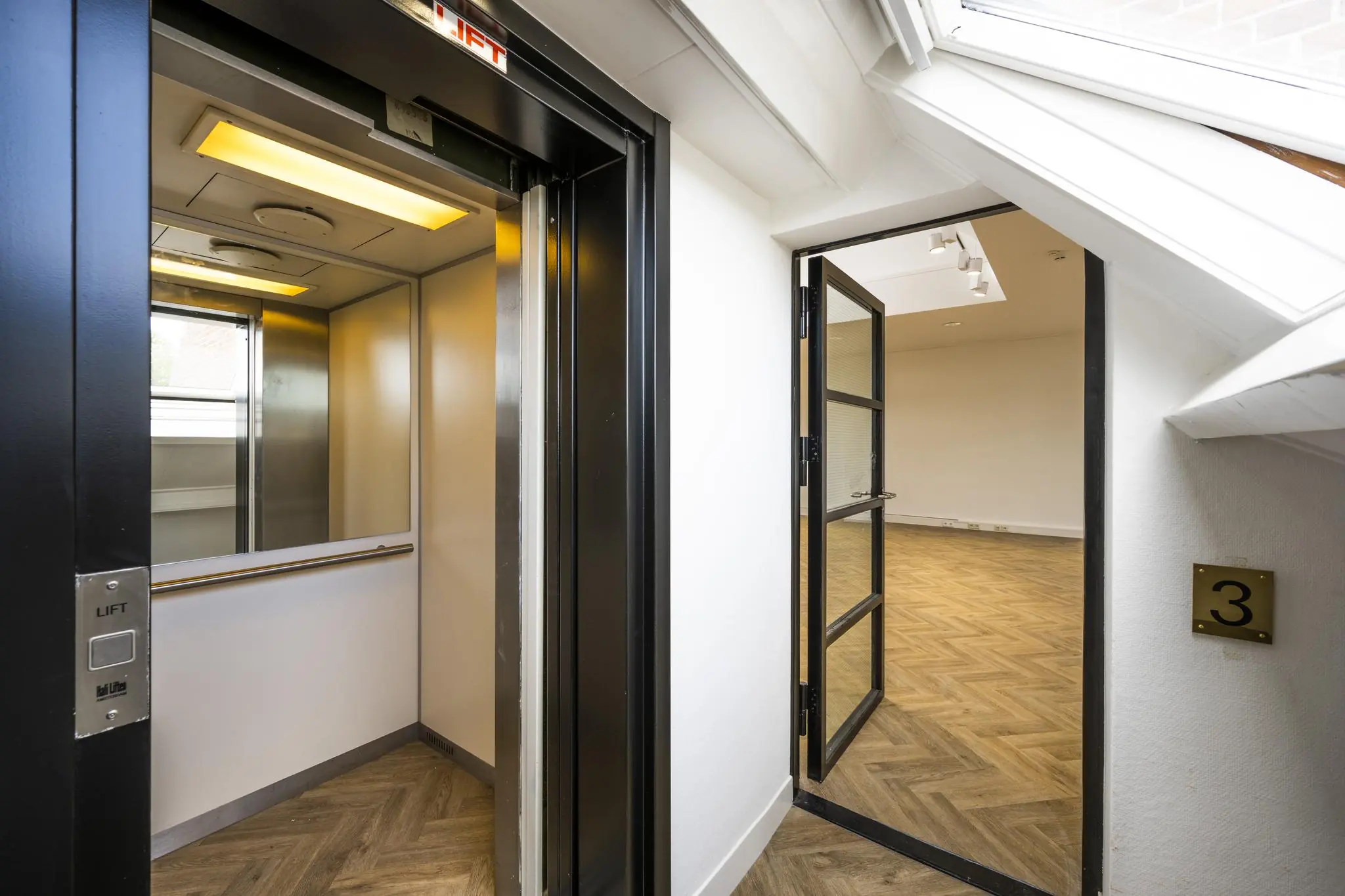 Open liftdeur en glazen deur naar een lege ruimte op de derde verdieping van een gebouw aan het Emmaplein.
