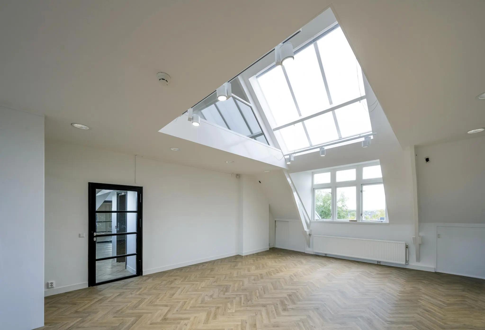 Lichte zolderruimte op het Emmaplein met visgraatvloer, dakramen en moderne zwarte binnendeur.
