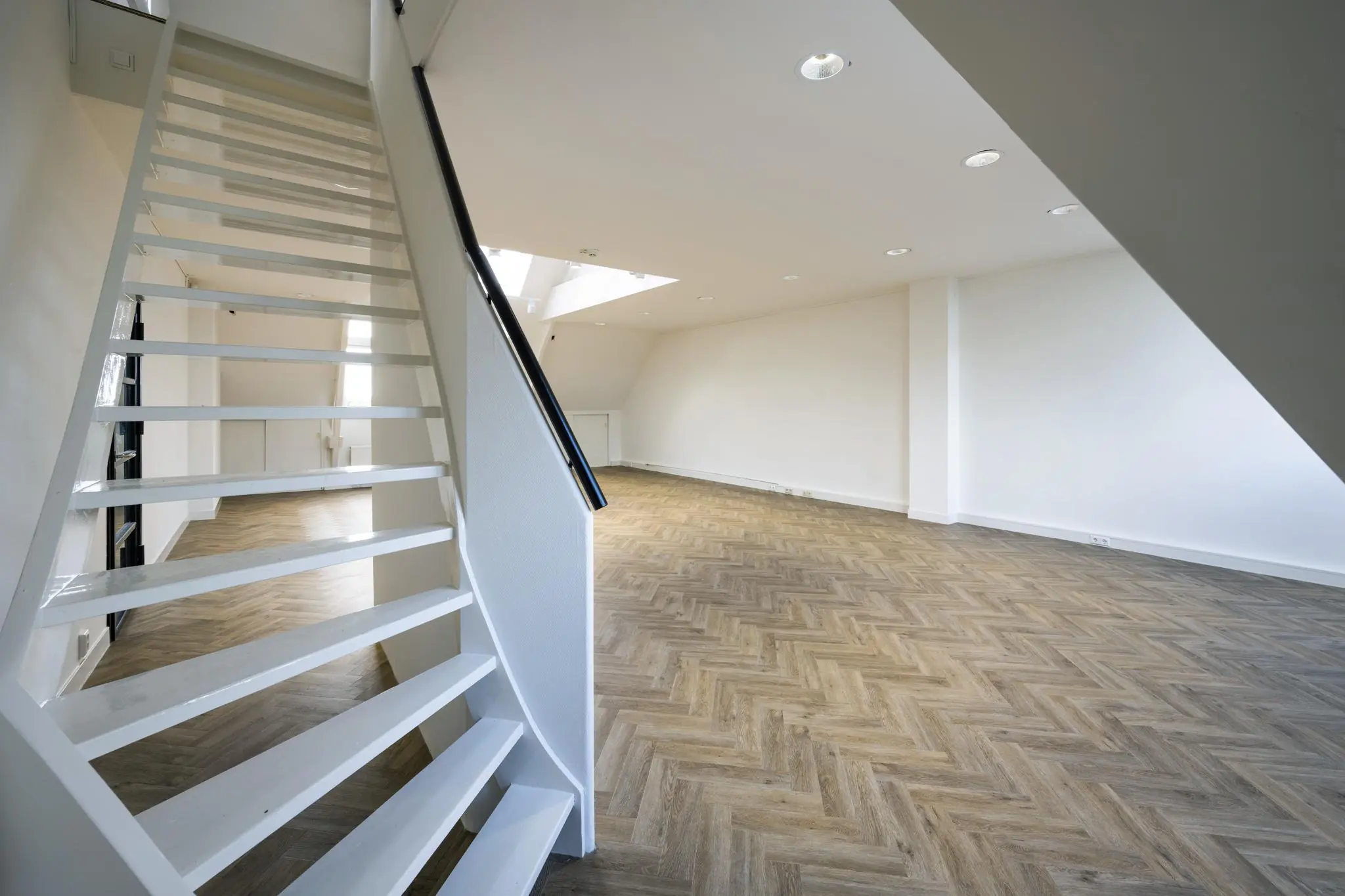 Lichte, lege ruimte aan het Emmaplein met visgraatvloer en witte open trap.