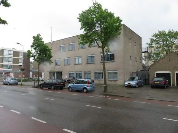 Een lichtbruinig kantoorgebouw aan de Nassaulaan met geparkeerde auto's en enkele bomen langs de straat.