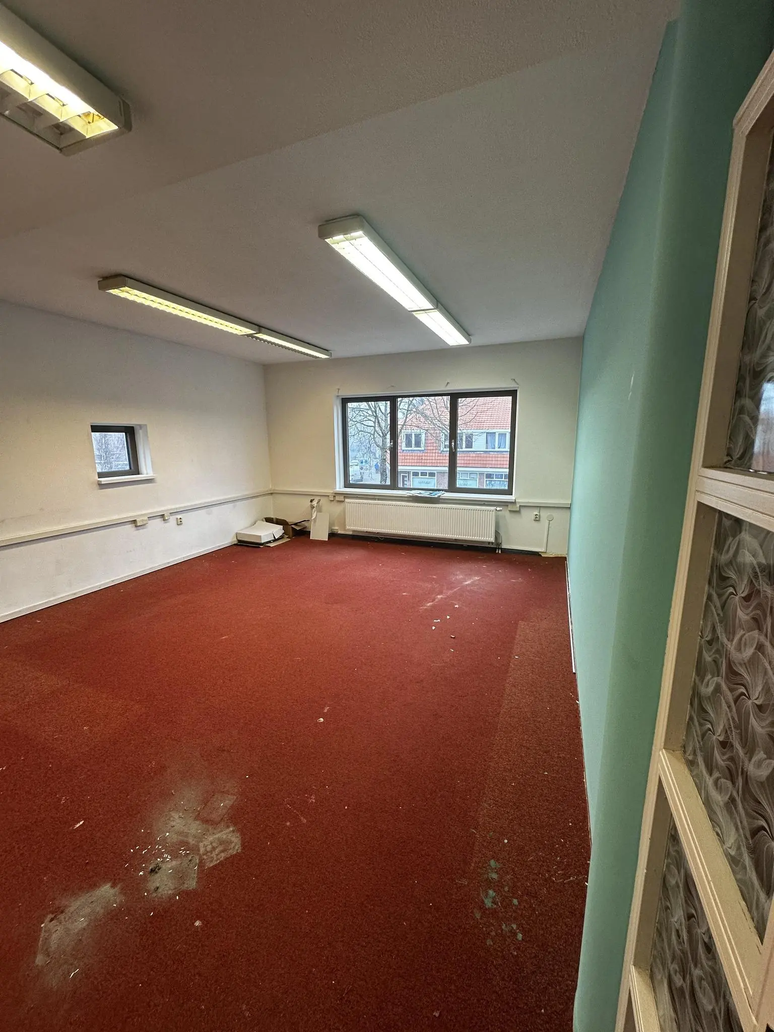 Lege kamer met rood tapijt, witte muren en een groot raam met uitzicht op de Nassaulaan.