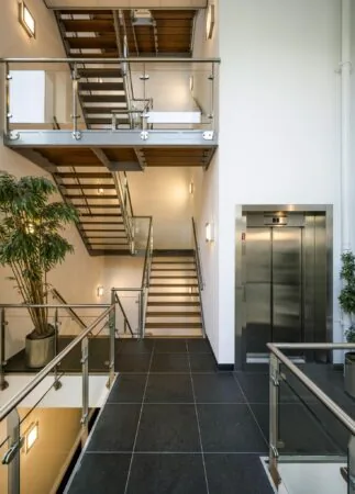 Moderne trappenhal met glazen balustrades, een metalen lift en grote planten aan de Sijsjesbergweg.