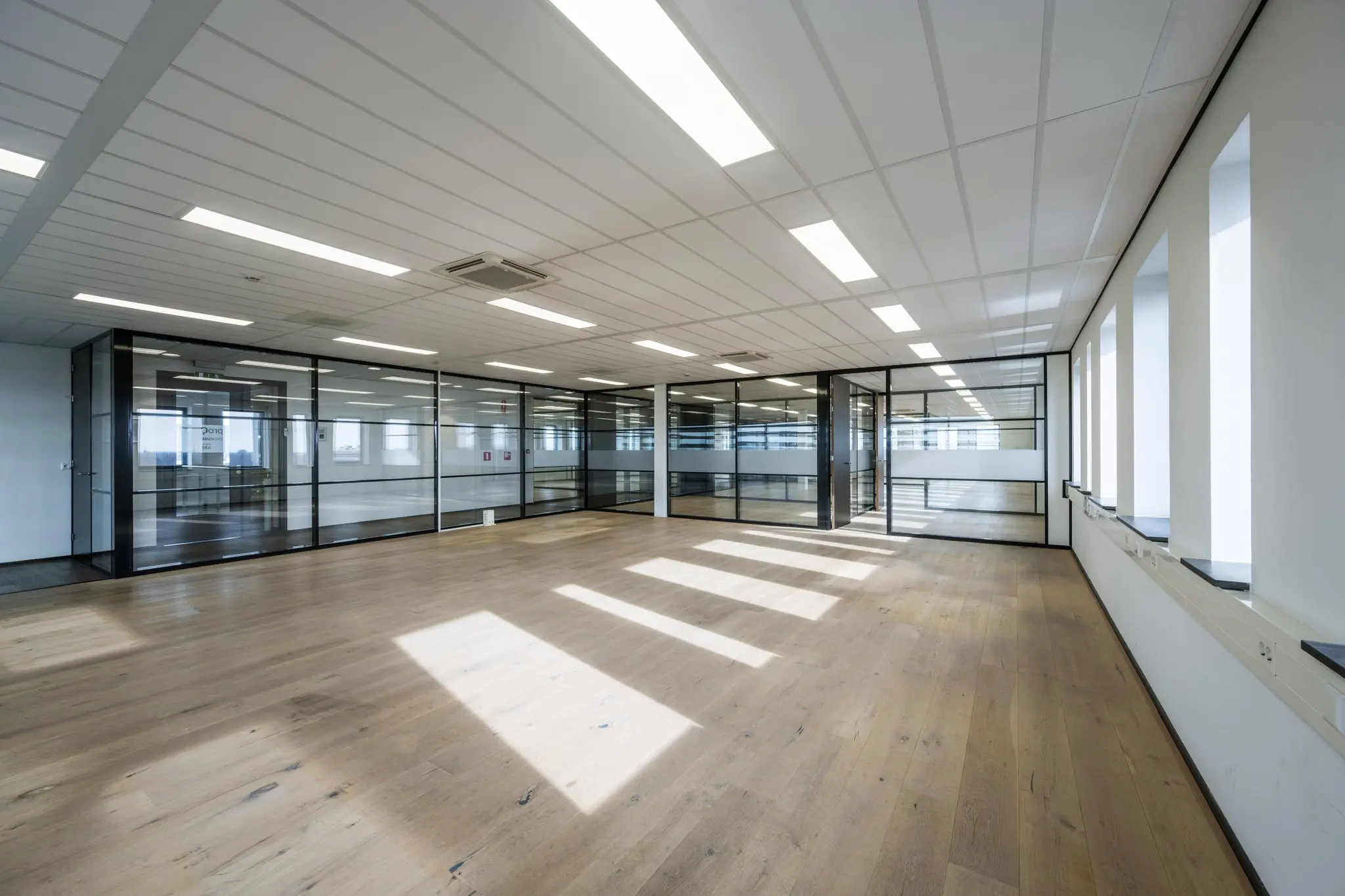 Lichte, ruime kantoorruimte aan de Sijsjesbergweg met glazen scheidingswanden, houten vloer en systeemplafond.