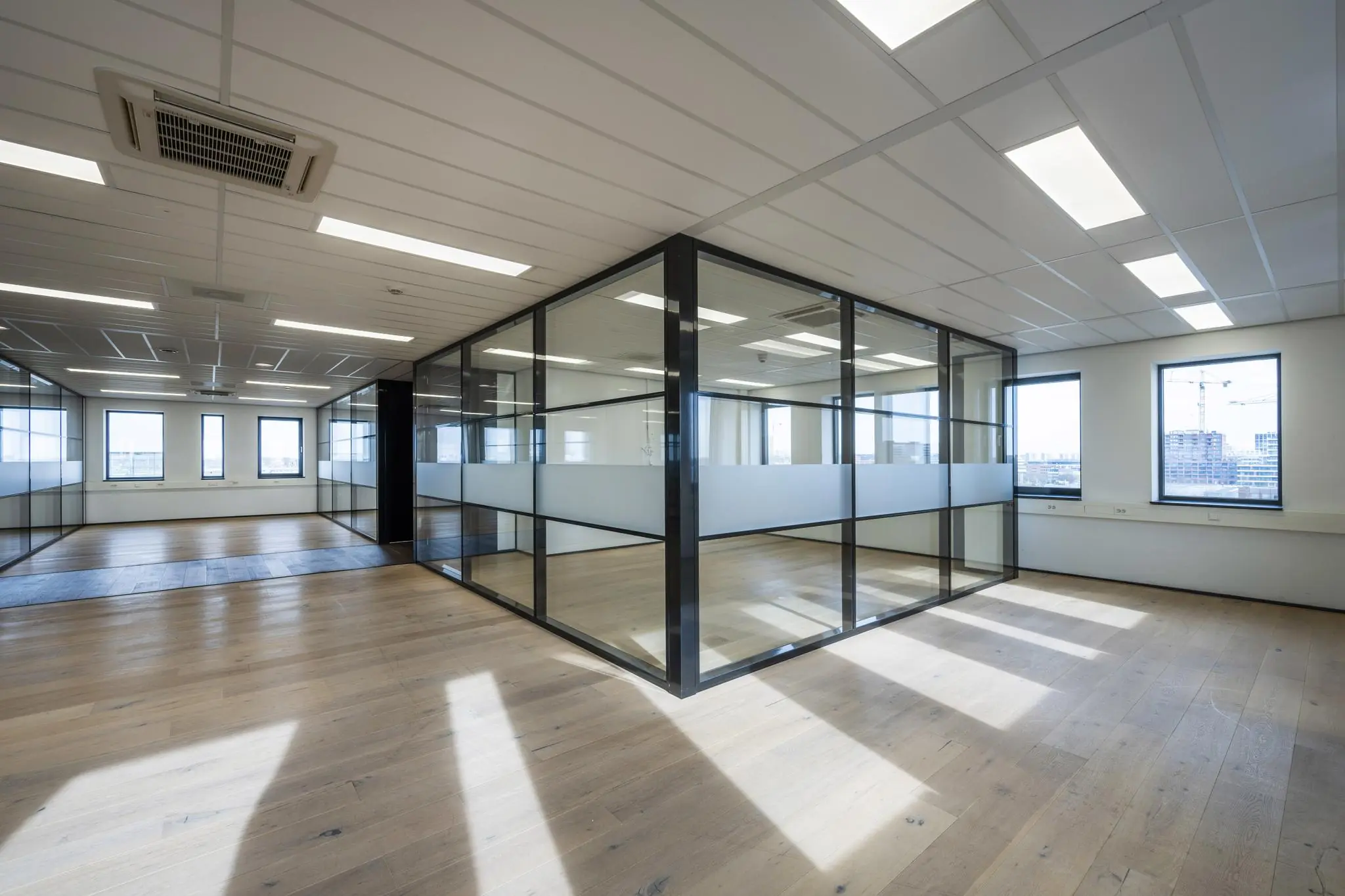 Modern en licht kantoorinterieur aan de Sijsjesbergweg met glazen vergaderruimtes en houten vloer.