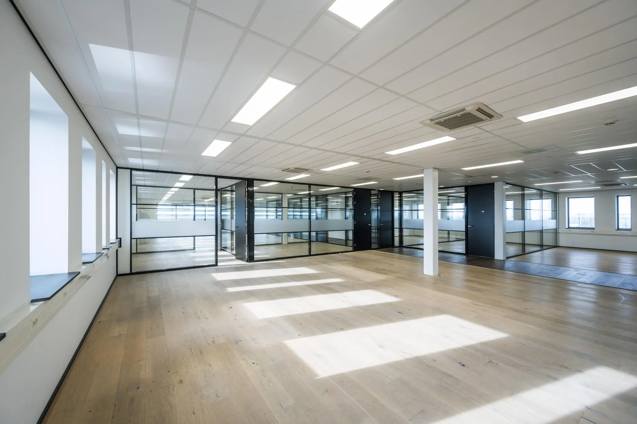 Licht, modern kantoorinterieur aan de Sijsjesbergweg met glazen wanden en houten vloer.