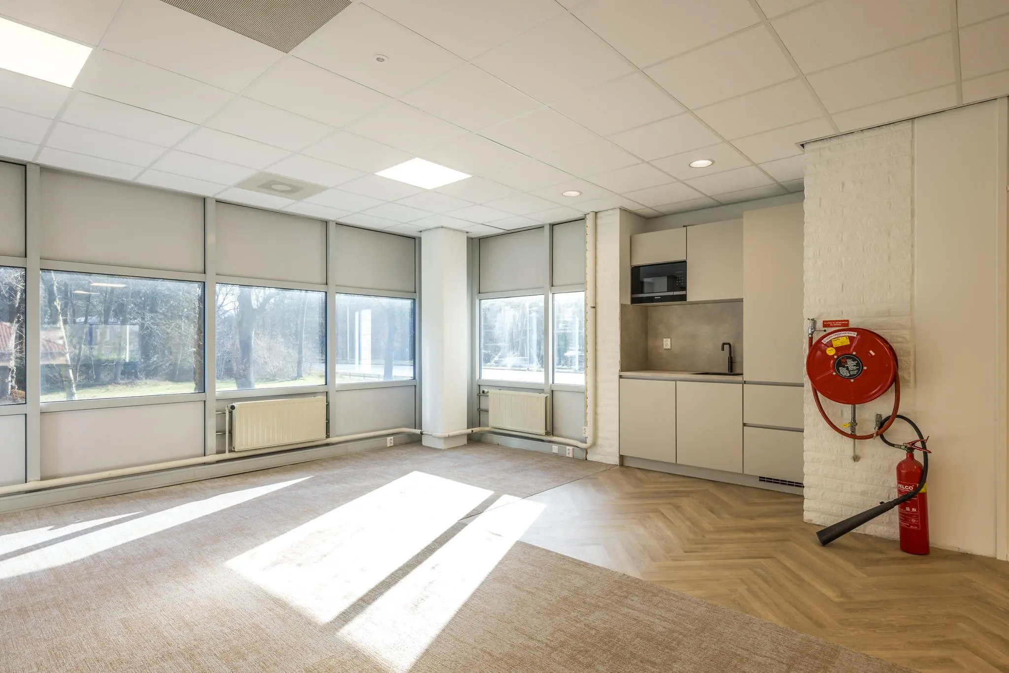 Lichte kantoorruimte aan de Dolderseweg met grote ramen, een moderne kitchenette en een brandslanghaspel aan de muur.