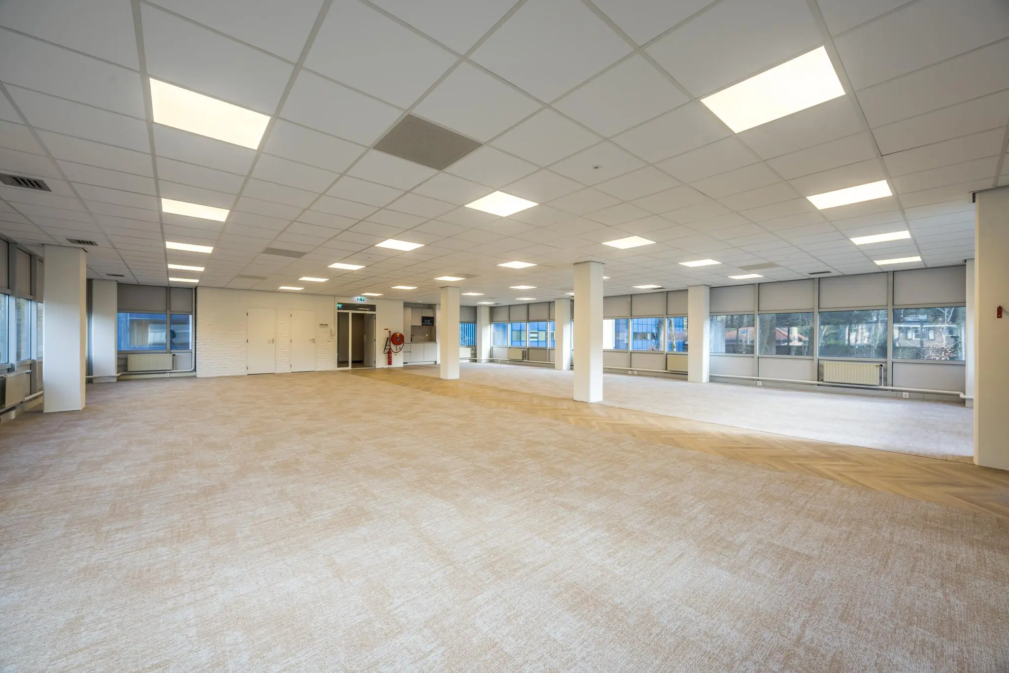 Ruime, lege kantoorruimte aan de Dolderseweg met systeemplafond, grote ramen en beige vloerbedekking.