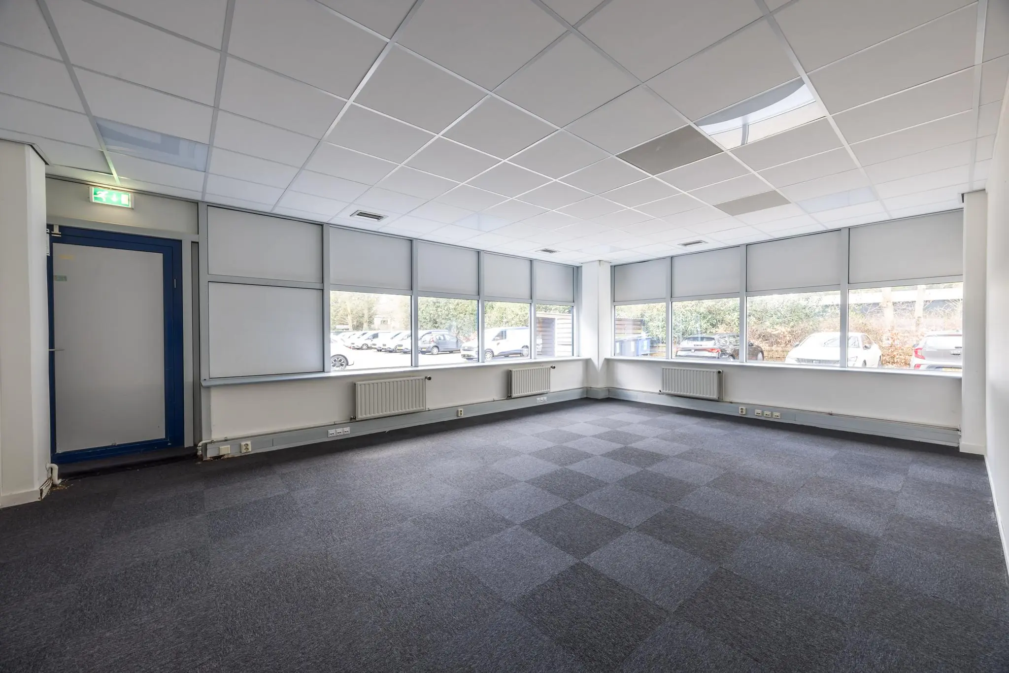 Lege kantoorruimte aan de Dolderseweg met tapijttegels, systeemplafond en grote ramen met zonwering.
