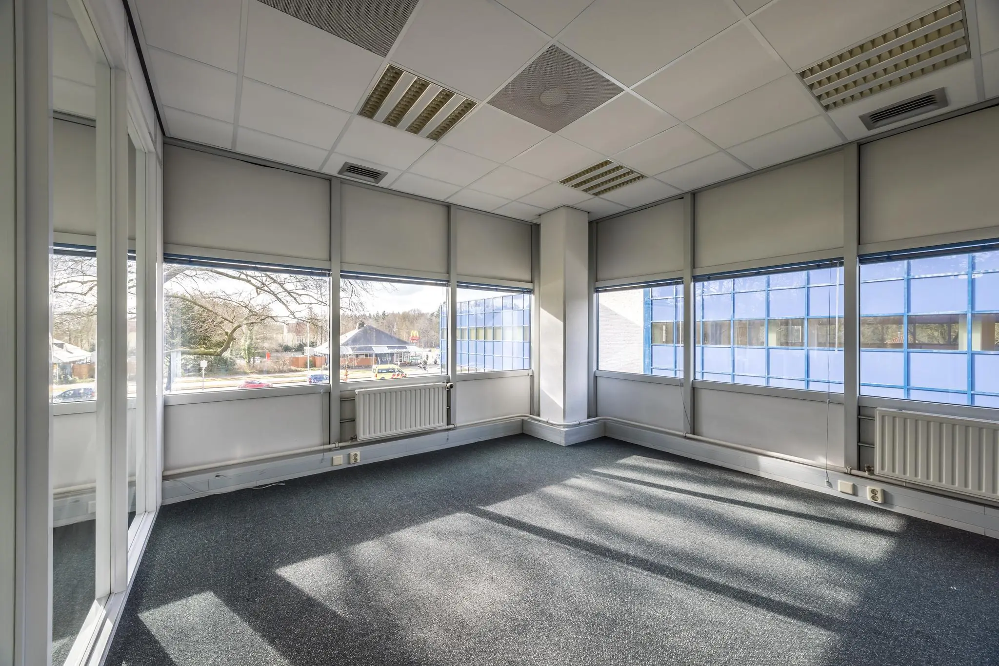 Licht en leeg hoekkantoor met grote ramen aan de Dolderseweg, uitzicht op straat en blauw kantoorgebouw.