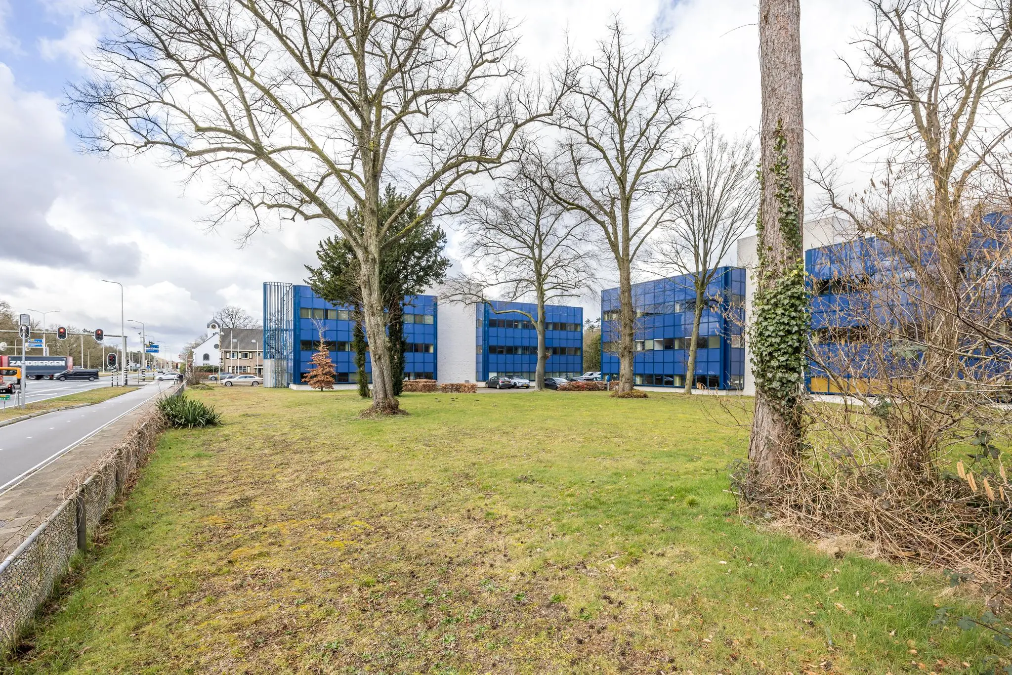 Kantoorgebouw met blauwe gevel aan de Dolderseweg, omringd door grasveld en bomen.