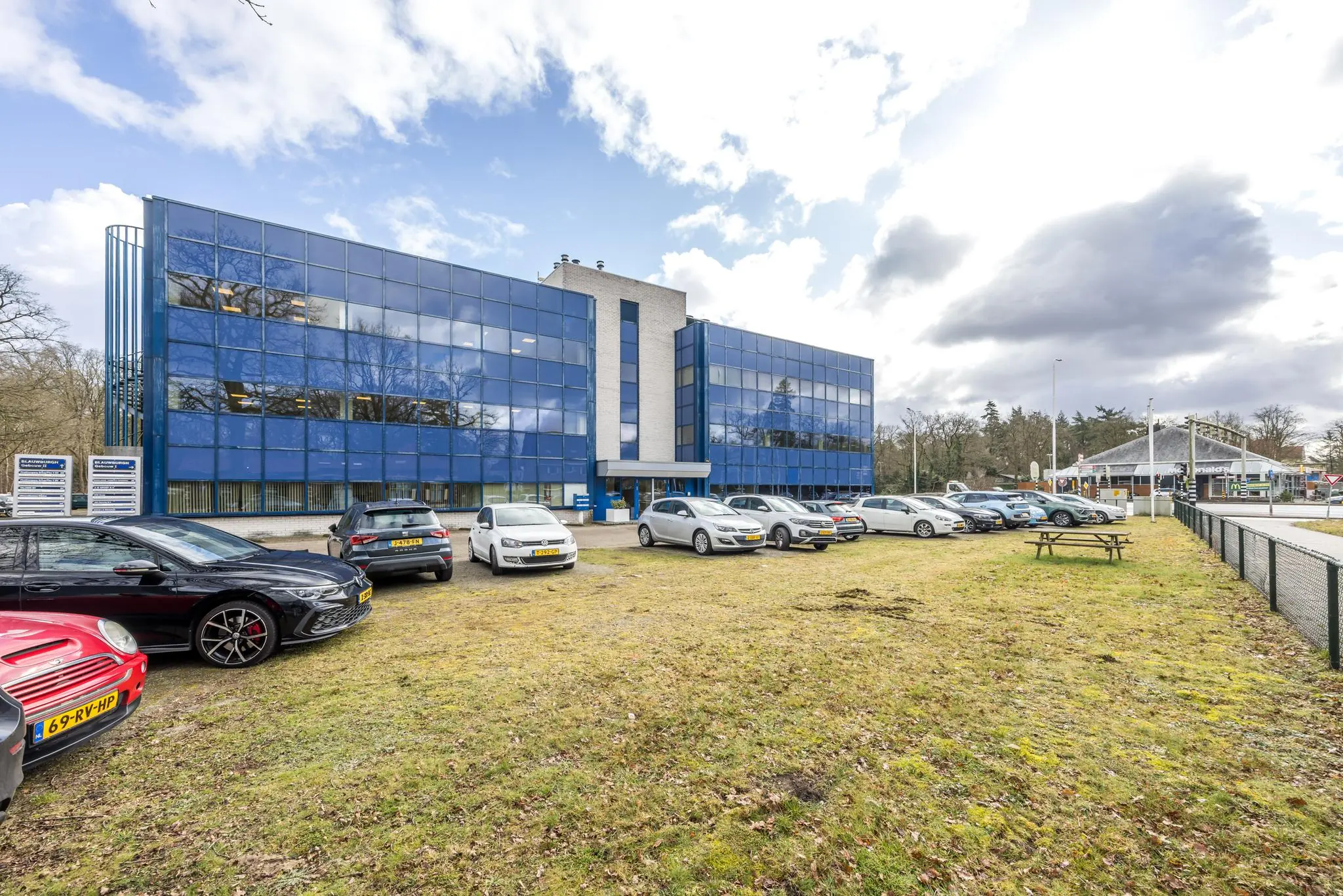 Kantoorgebouw aan de Dolderseweg met spiegelende blauwe gevel en parkeerplaats vol auto's op de voorgrond.