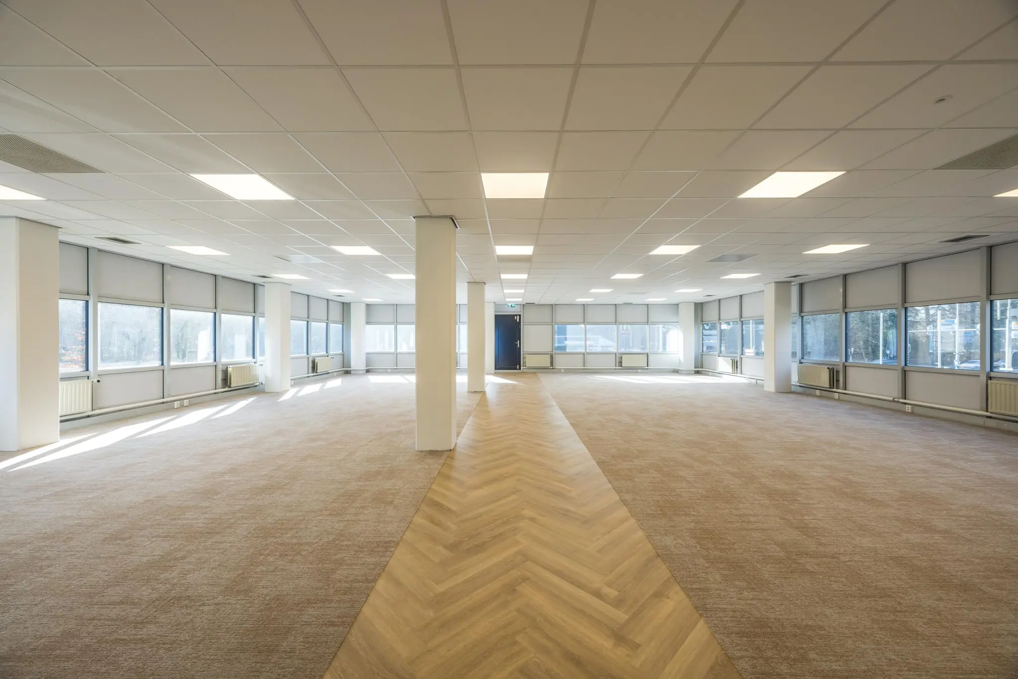 Ruime, lege kantoorruimte aan de Dolderseweg met grote ramen, systeemplafond en een visgraatvloerpad in het midden.