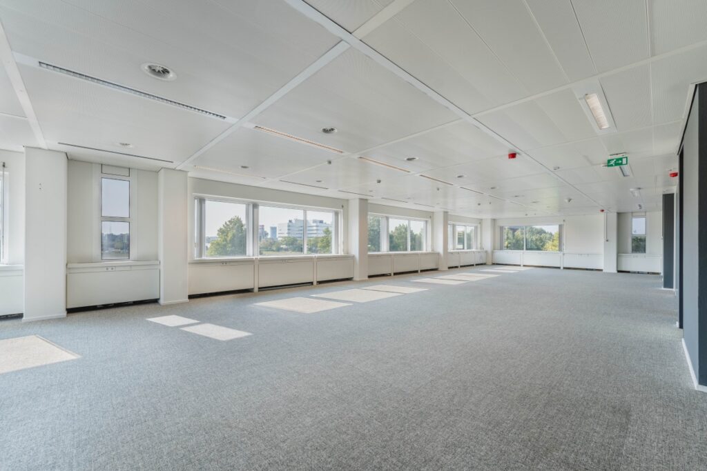 Lichte, lege kantoorruimte aan de Laarderhoogtweg met grote ramen en grijze vloerbedekking.
