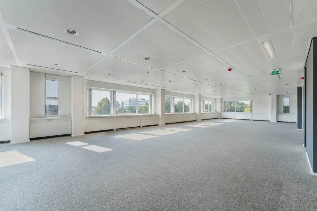Lichte, lege kantoorruimte aan de Laarderhoogtweg met grote ramen en grijze vloerbedekking.