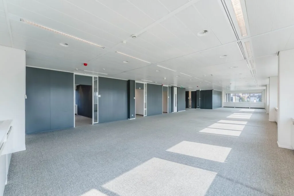 Ruim en licht kantoorinterieur aan de Laarderhoogtweg met grijze vloerbedekking en witte systeemplafonds.