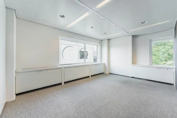 Lichte, lege kantoorruimte aan de Laarderhoogtweg met grote ramen en grijze vloerbedekking.