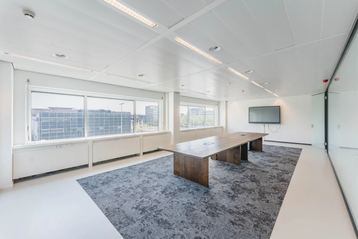 Moderne vergaderruimte aan de Laarderhoogtweg met grote ramen, houten vergadertafel en een muurmonitor.